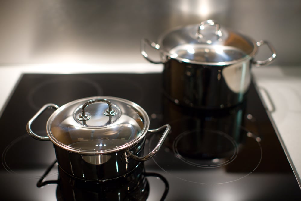 Two gleaming stainless steel saucepans placed on a black glass top electric stove.