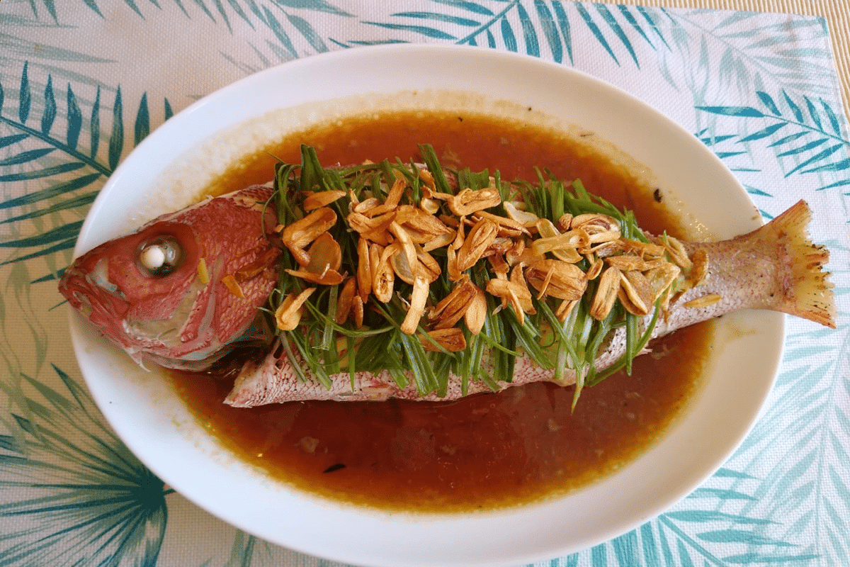 A freshly steamed red snapper garnished with roasted garlic and green onions.