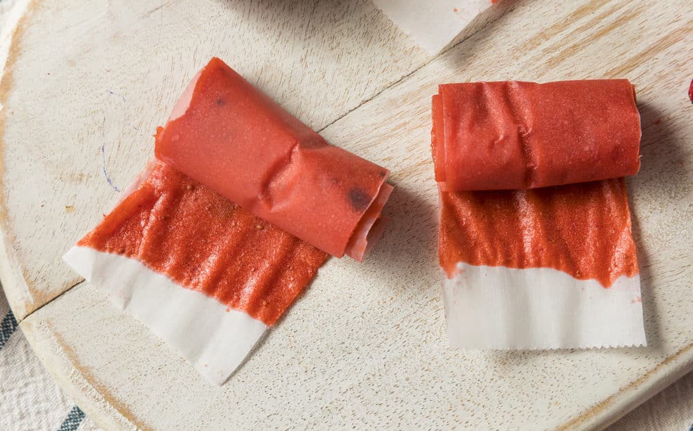 Strawberry fruit leather rolls neatly arranged on a wooden cutting board.