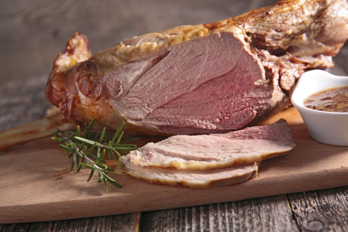 Sliced roast leg of lamb on a wooden board with rosemary garnishing