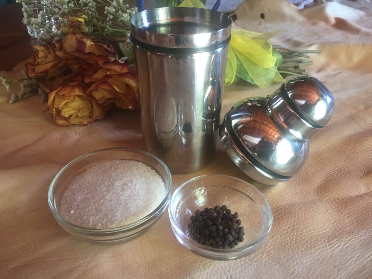 Clear bowls containing sugar and peppercorns beside a shaker and decorative flowers.