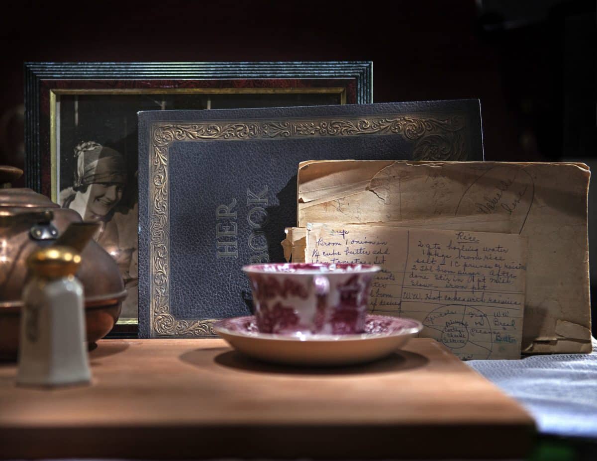 Vintage teacup beside an old recipe card and blue cookbook on a wooden table.