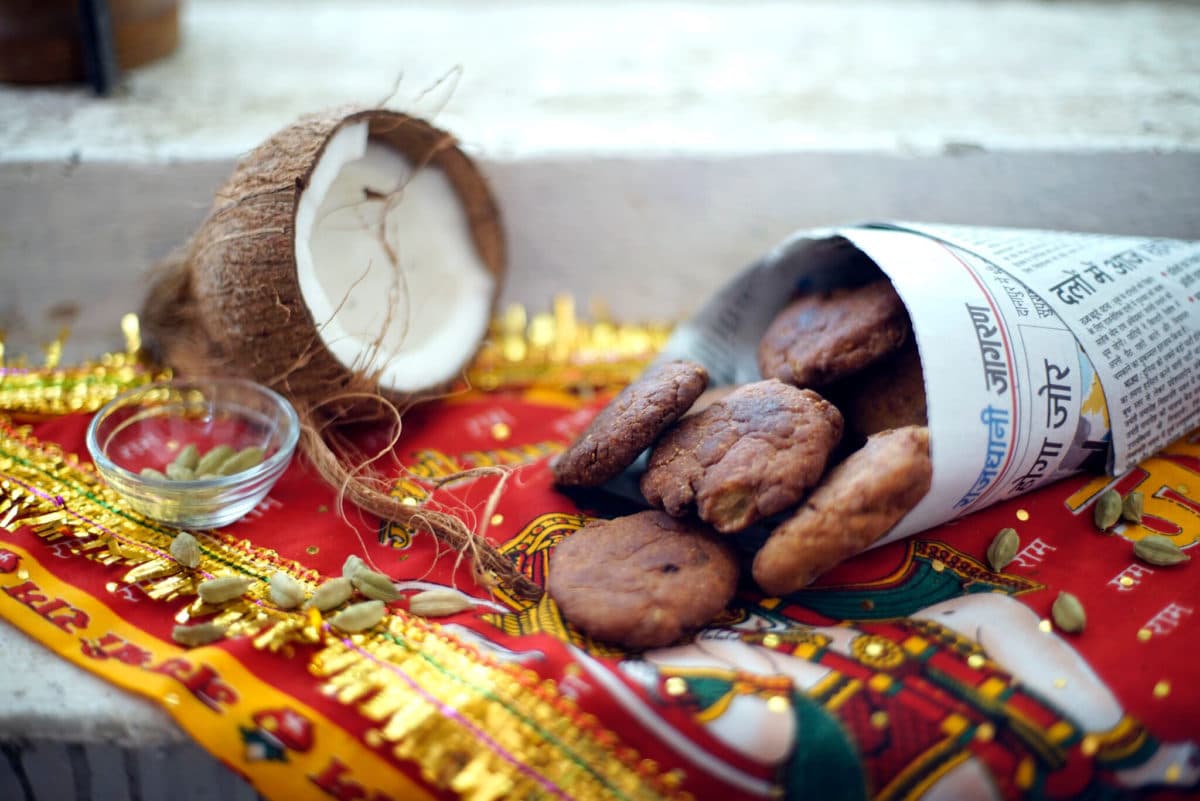 Thekua cookies on a decorative blanket with a split-open coconut and newspaper cone.