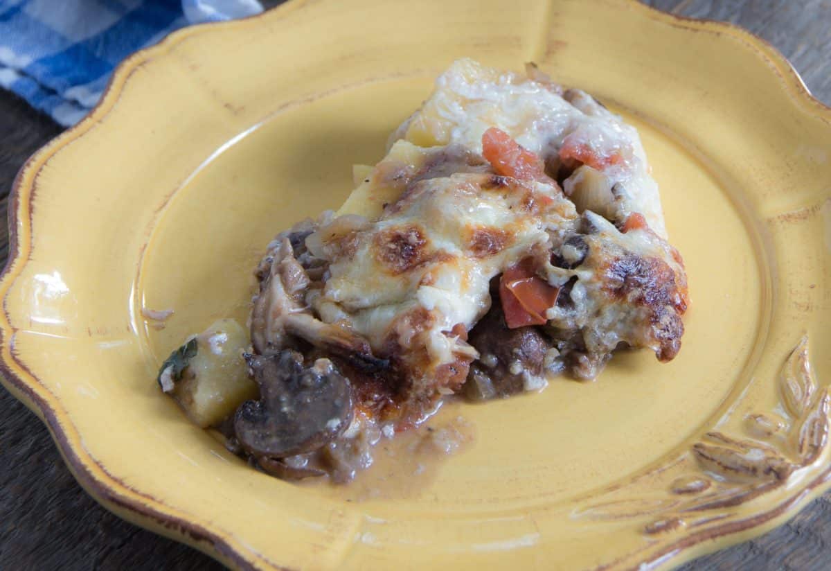 A serving of three-cheese polenta pie with mushrooms and tomatoes on a yellow plate.
