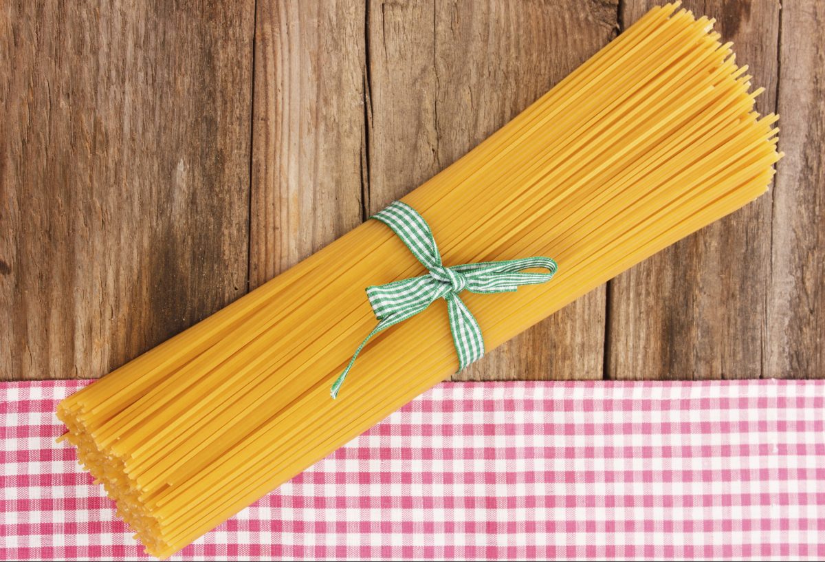 Uncooked spaghetti tied neatly with a green bow on a checkered tablecloth.