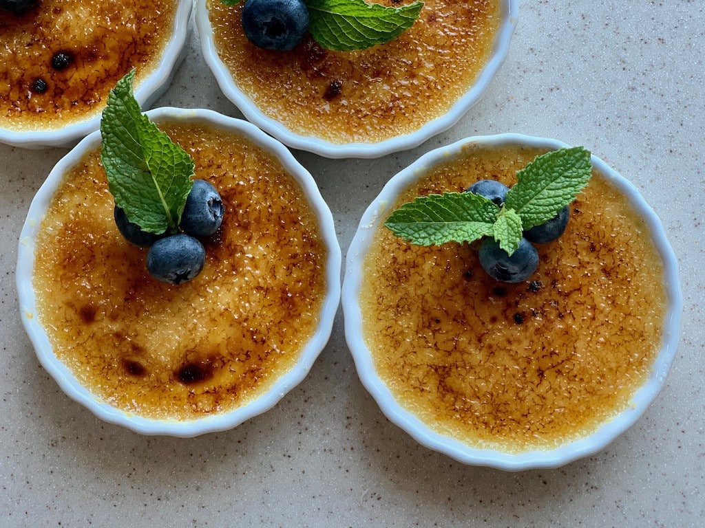 Top view of a crème brûlée garnished with blueberries and mint leaves