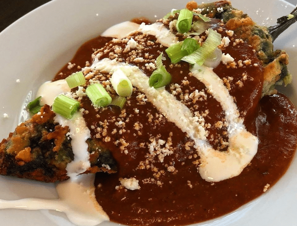 A mouth-watering Chile Relleno topped with sauce, cream, and green onions.