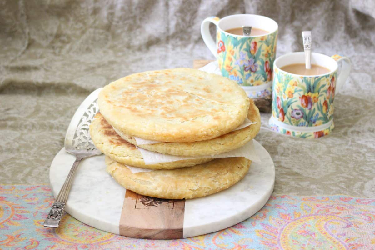 Two cups of tea next to flatbread on floral tablecloth.