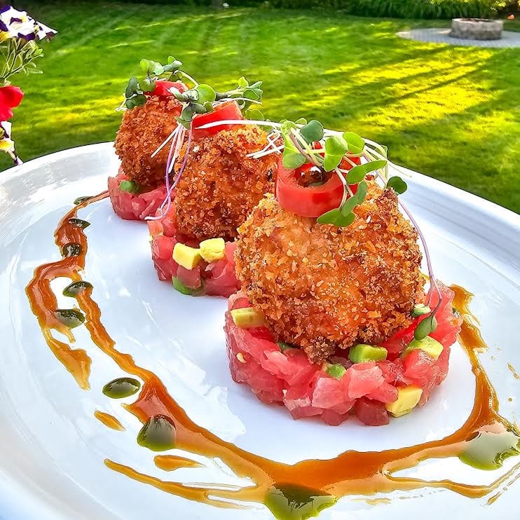 Golden croquettes placed on a bed of diced tuna, garnished with microgreens and a drizzle of sauce.