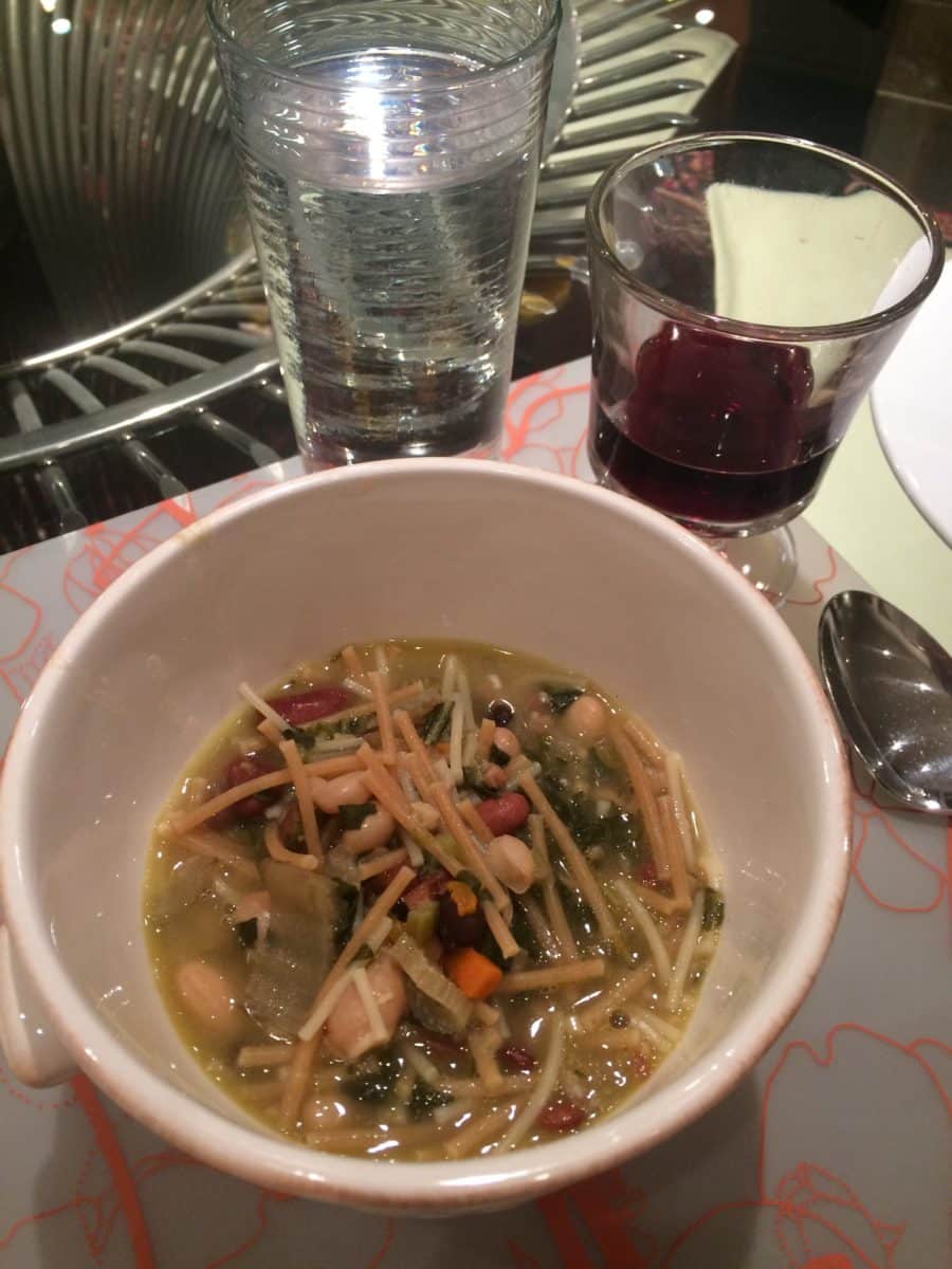 A bowl of Tuscan-style pasta e fagioli soup accompanied by a glass of water and a glass of red drink.