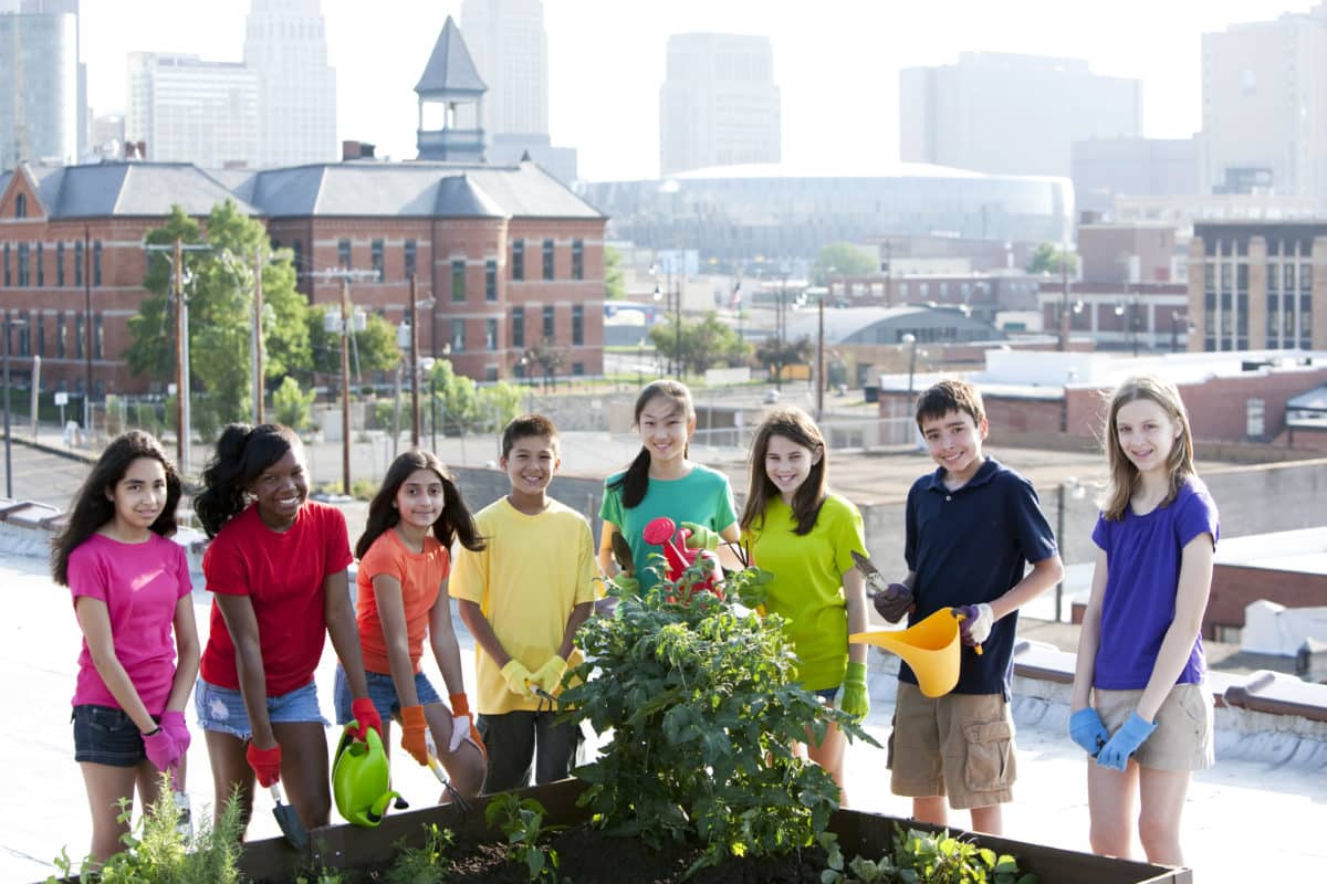 Diverse group of eight children tending to an urban rooftop garden.