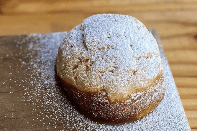 A vanilla concha pastry sprinkled with powdered sugar on a wooden table.