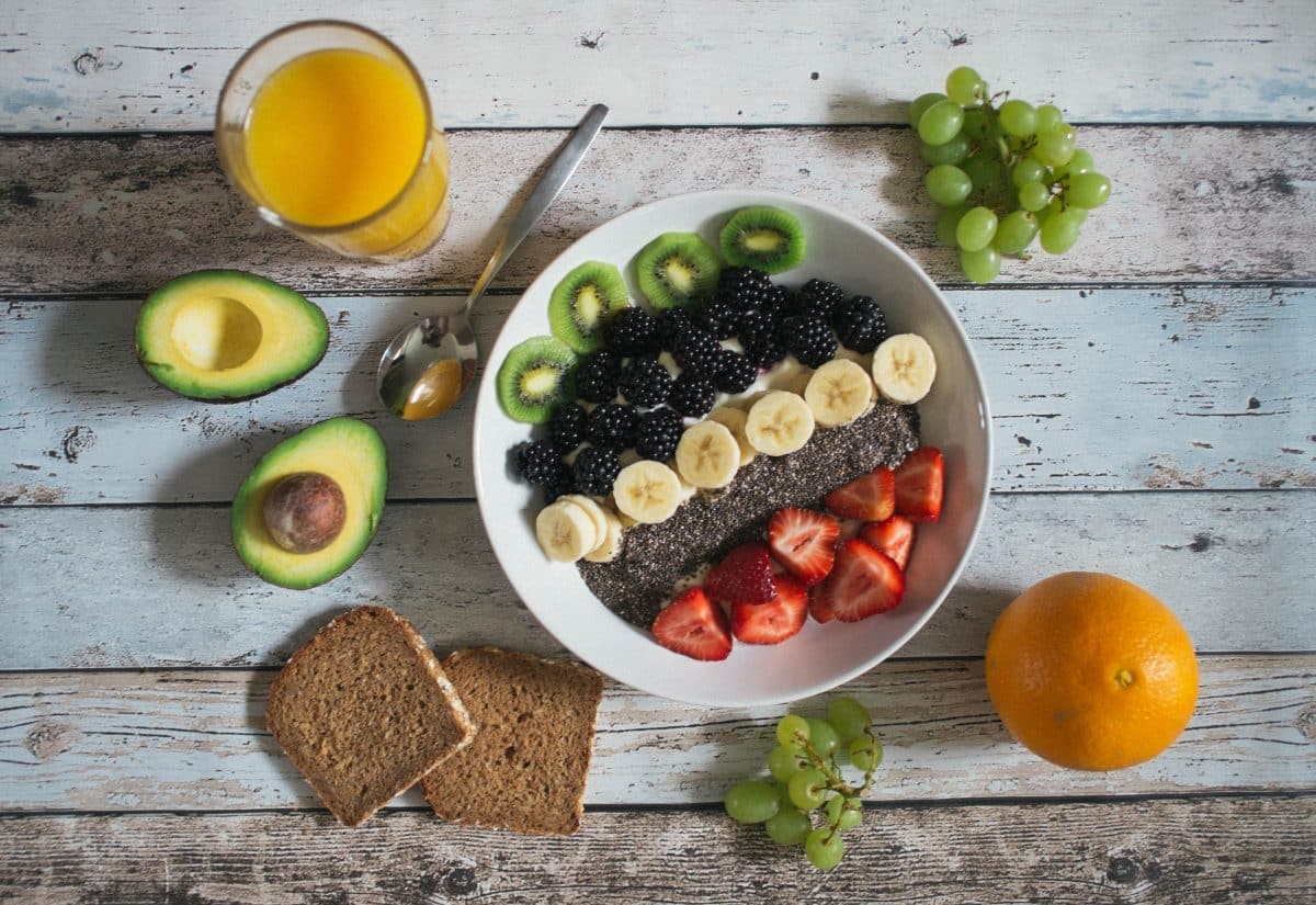A breakfast bowl filled with fresh fruits, chia seeds, bread, and a glass of orange juice.