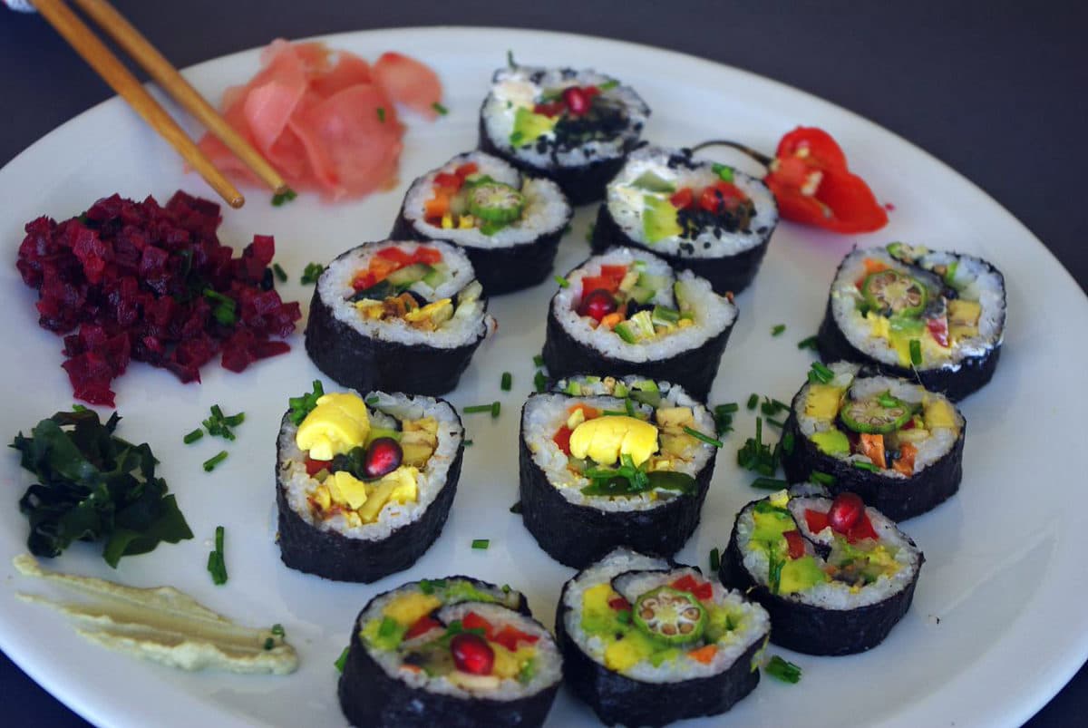 A plate of colorful vegan sushi with wasabi, ginger, and garnishes.