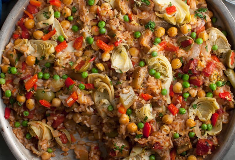 Close-up of vegetable paella with rice, peas, artichokes, and red pepper
