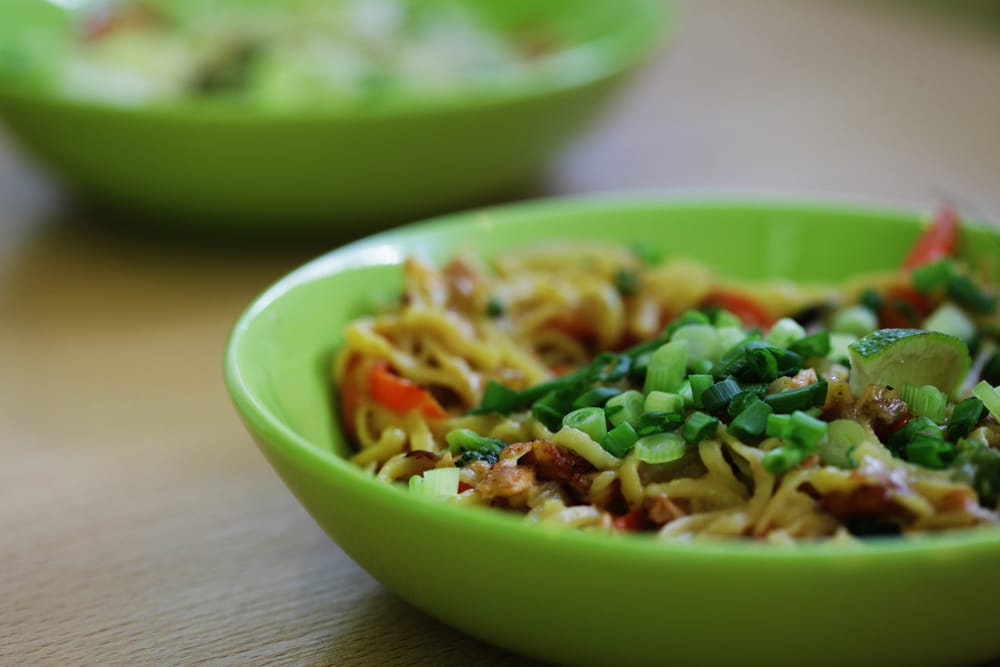 Bowl of rice noodles mixed with fresh chopped vegetables.