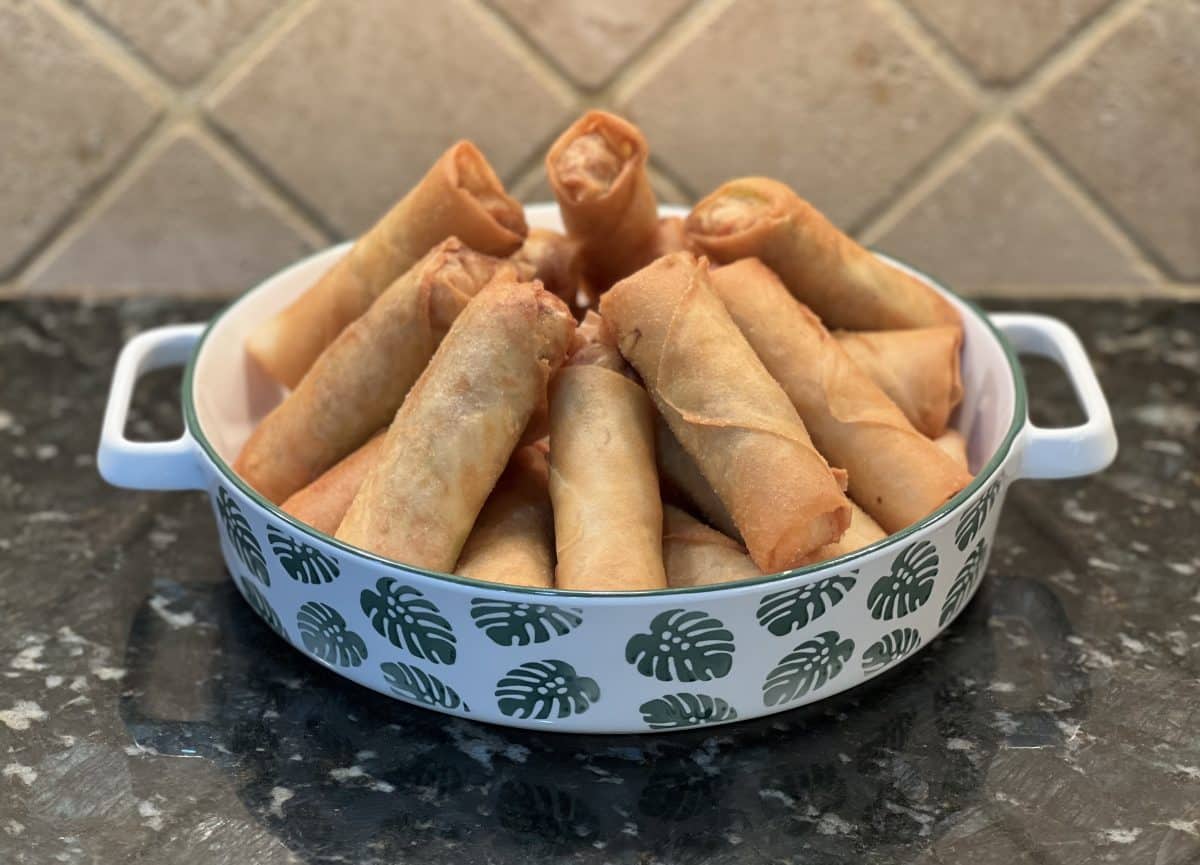 A bowl of fried spring rolls with a leafy pattern on the bowl.