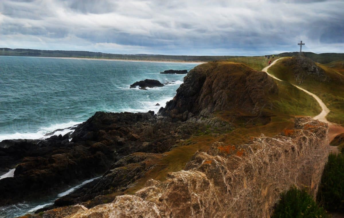 Coastal view of Wales with a cross on a hill in the distance.