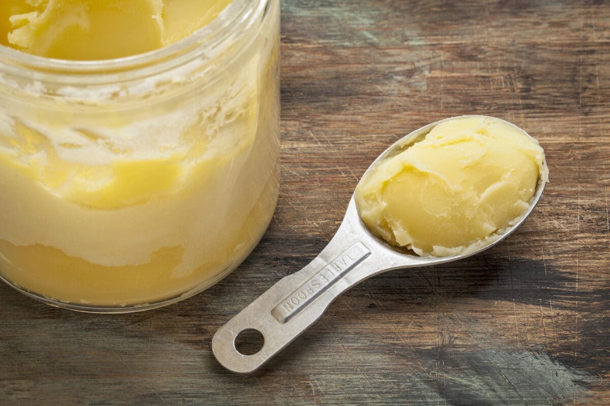 jar of ghee with measuring spoon on wooden table