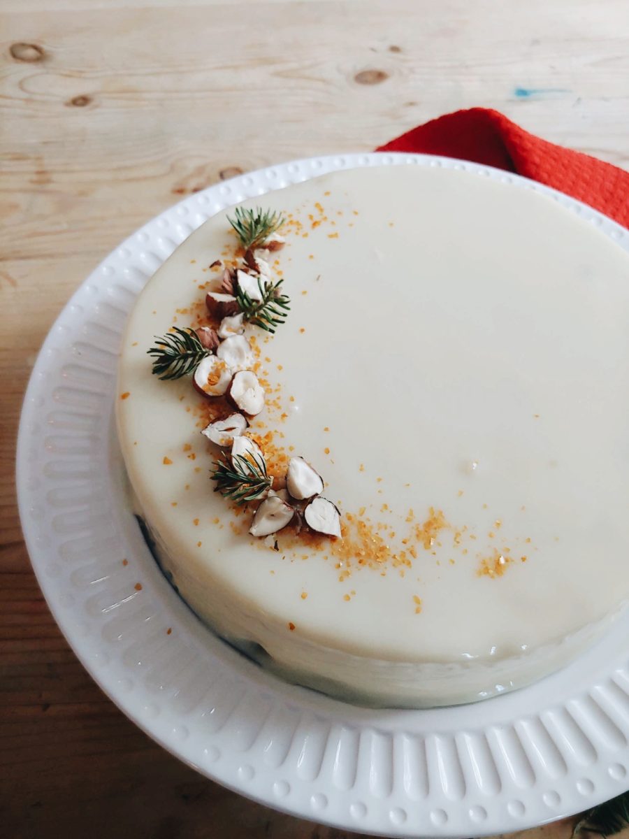 A white chocolate mousse cake decorated with sprigs of pine and sprinkled hazelnuts.
