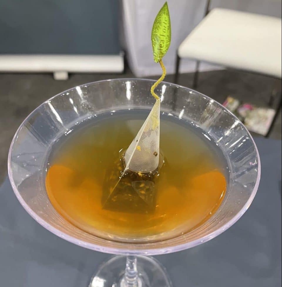A martini glass with a tea bag infuser and golden liquid.