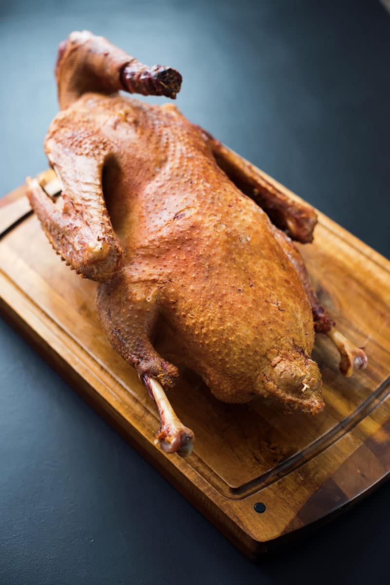 Whole smoked duck with sliced wing and breast, presented on a wooden tray.