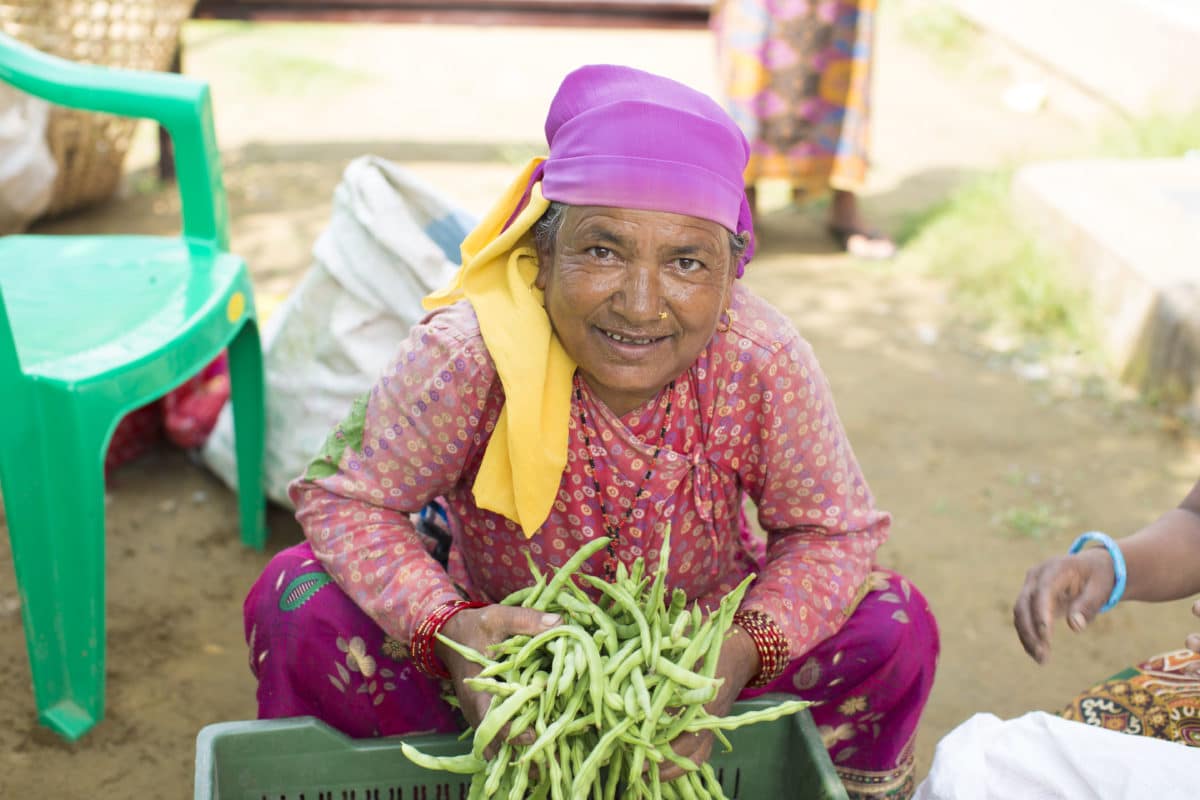 A woman in vibrant clothing sorting fresh green produce.