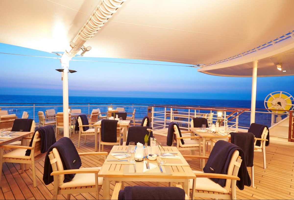 Outdoor seating area with wooden tables and chairs on the terrace of the Yacht Club on Europa 2